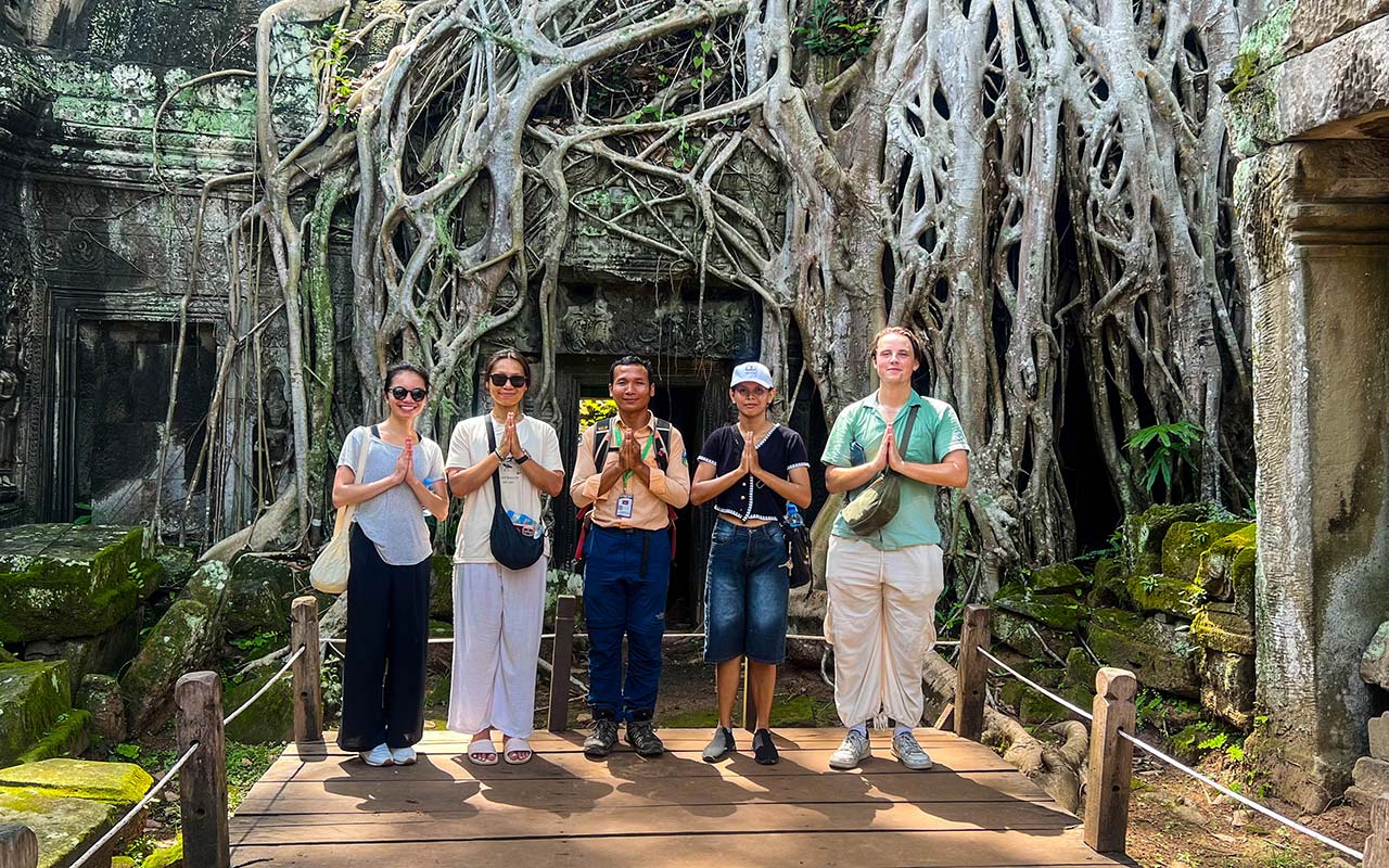 Chum, guide francophone certifié avec un groupe de touristes devant les racines géantes du temple de Ta Prohm à Angkor.