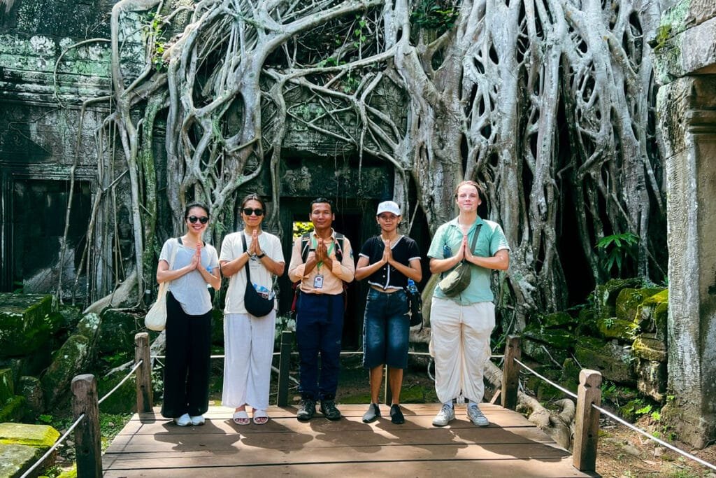 Chum, guide francophone certifié avec un groupe de touristes devant les racines géantes du temple de Ta Prohm à Angkor.