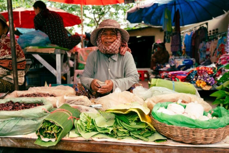 Vendeuse au marché traditionnel de Roluos présentant des feuilles de bétel, des légumes frais et des produits locaux près des temples de Roluos, à Siem Reap