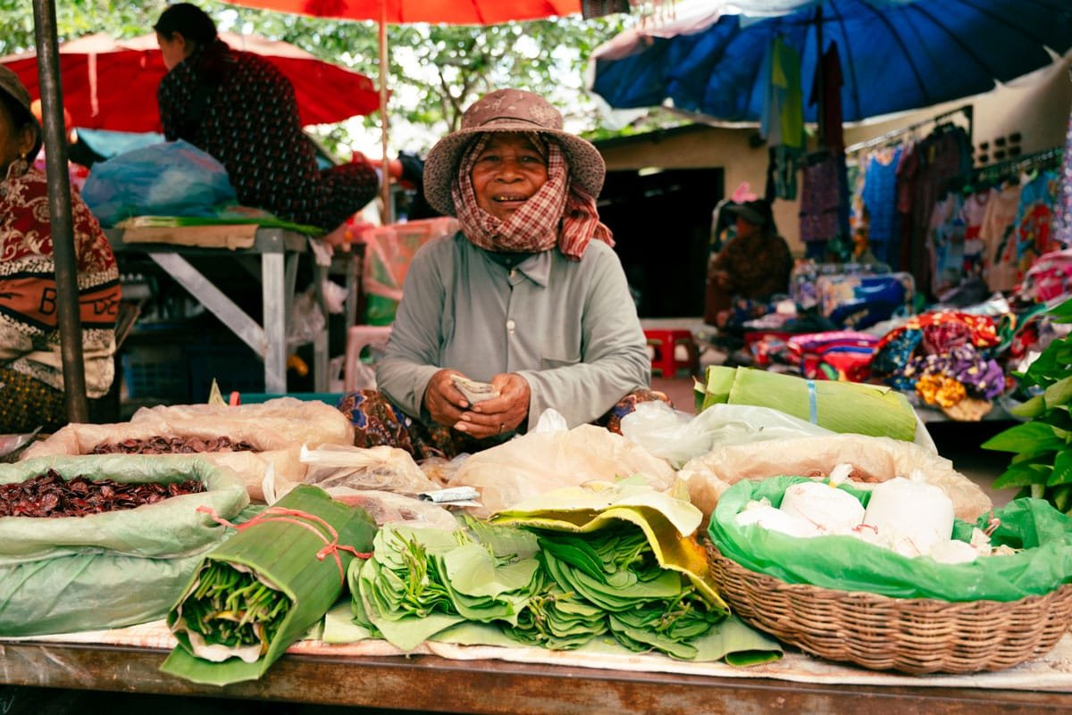 Vendeuse au marché traditionnel de Roluos présentant des feuilles de bétel, des légumes frais et des produits locaux près des temples de Roluos, à Siem Reap