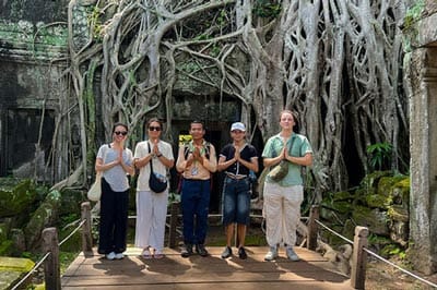 Chum, guide francophone certifié avec un groupe de touristes devant les racines géantes du temple de Ta Prohm à Angkor.